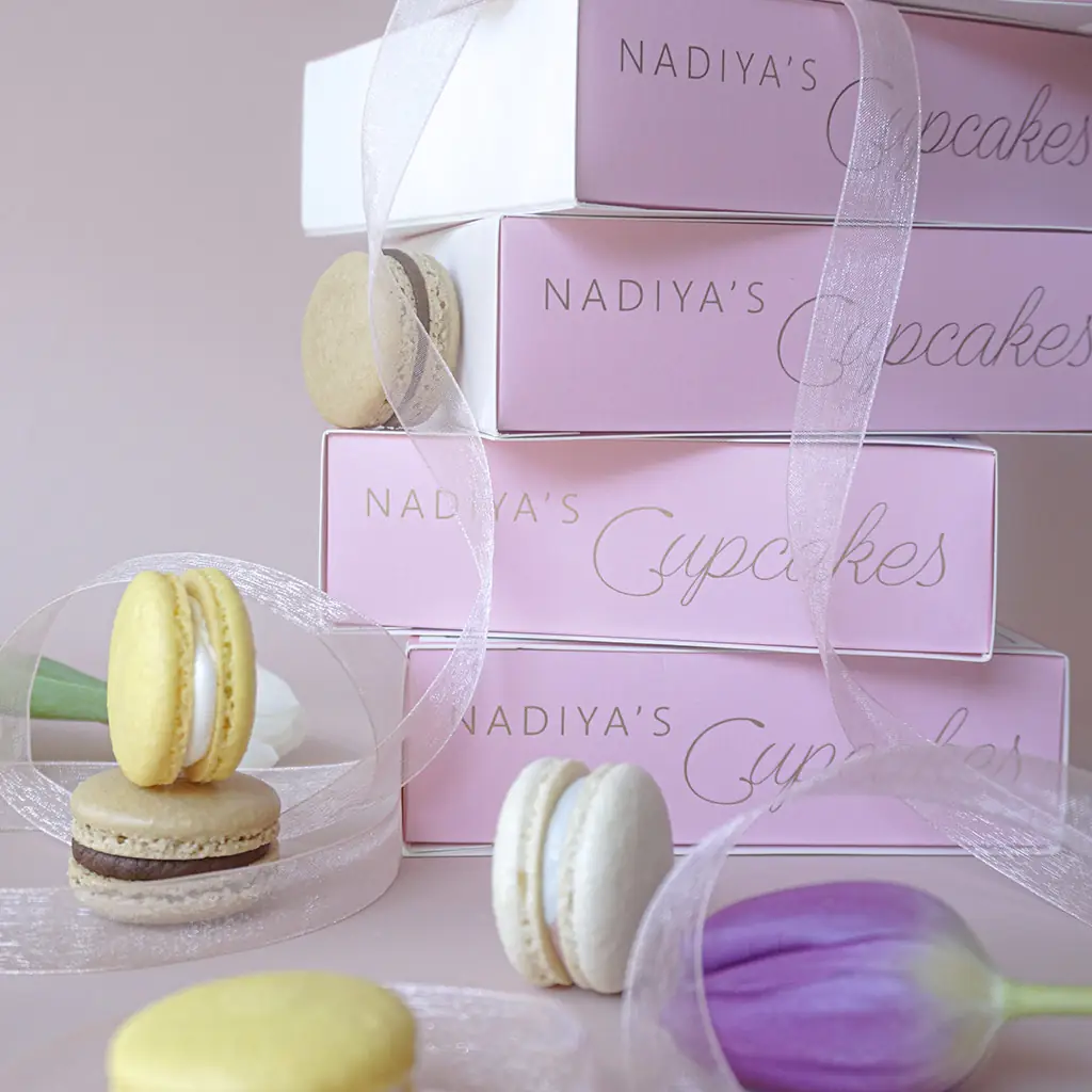Stacked boxes of macarons with pastel purple tulip nearby, by Nadiya's Cupcakes