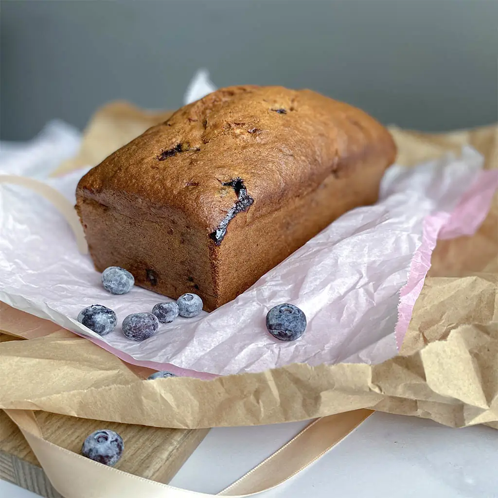 Whole loaf of blueberry banana bread on parchment paper, by Nadiya's Cupcakes