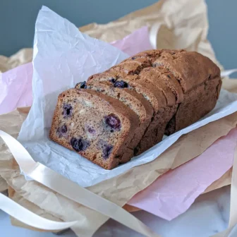 Loaf of blueberry banana bread sliced on parchment paper, by Nadiya's Cupcakes
