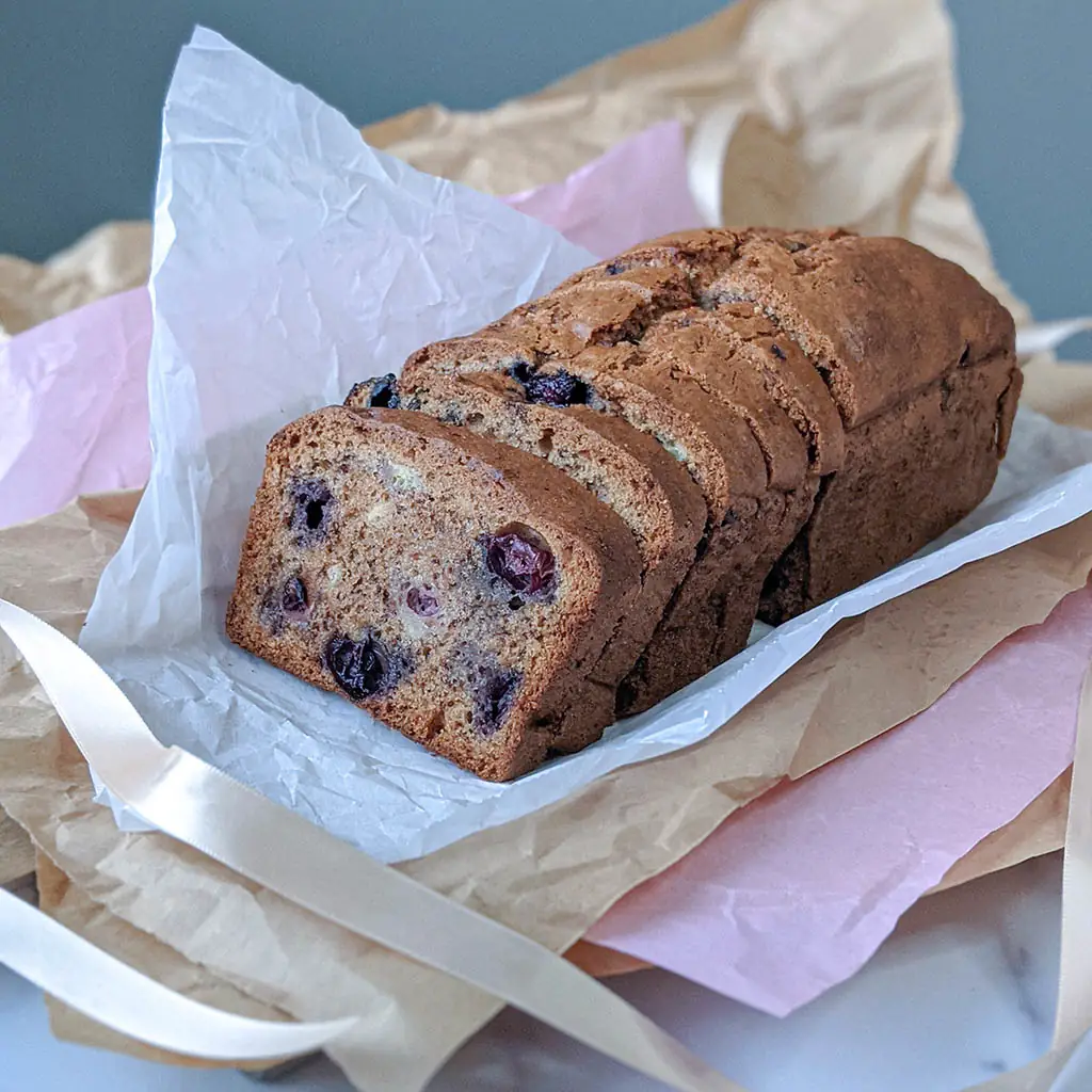 Loaf of blueberry banana bread sliced on parchment paper, by Nadiya's Cupcakes