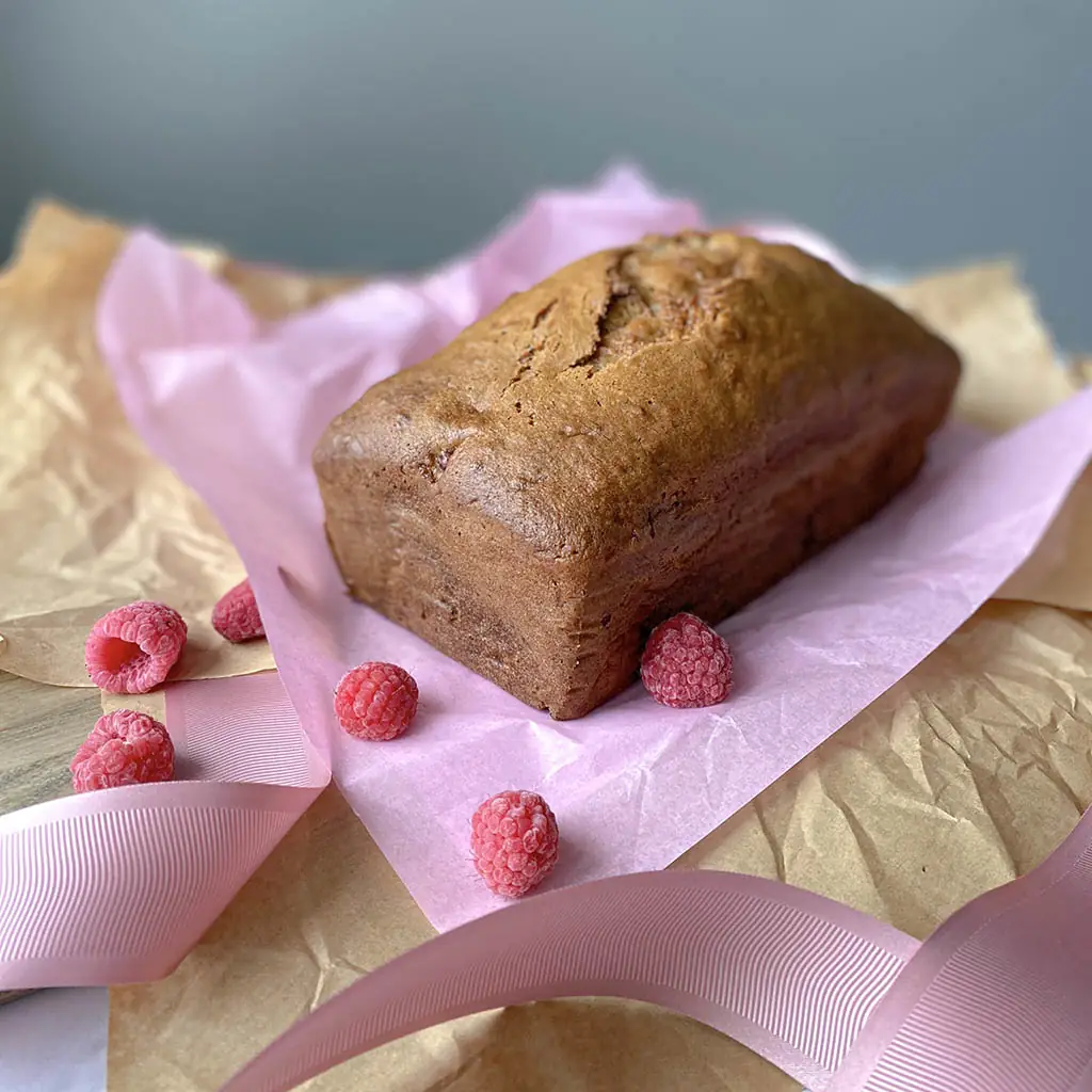 Whole loaf of raspberry banana bread on parchment paper, by Nadiya's Cupcakes