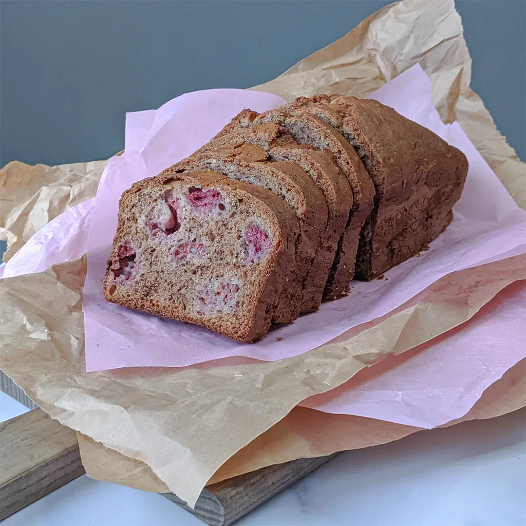 Loaf of raspberry banana bread sliced on parchment paper, by Nadiya's Cupcakes