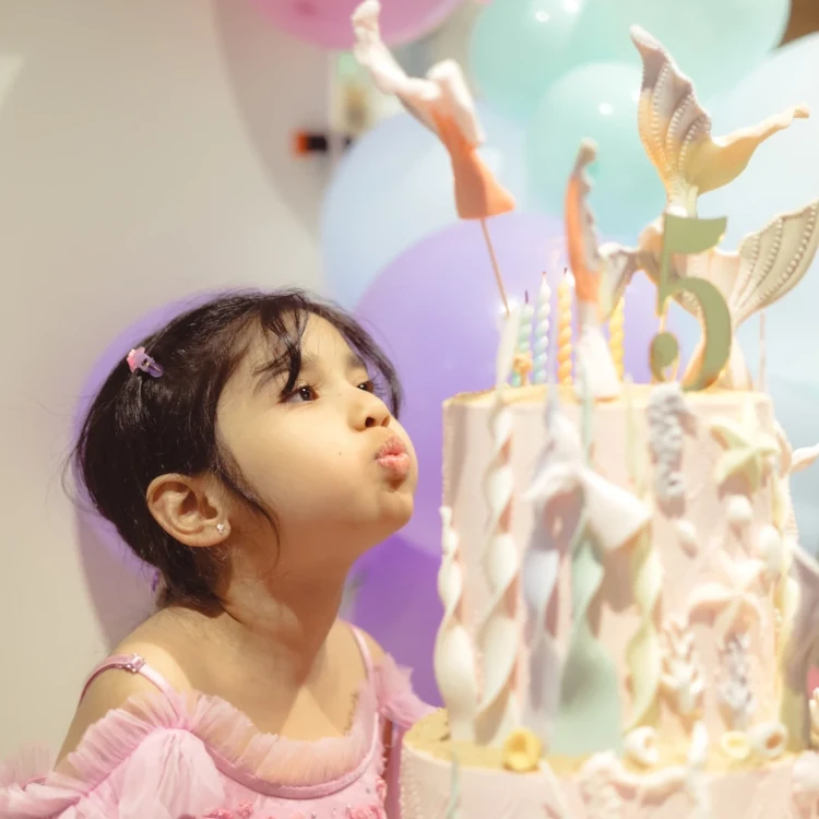 Young girl blowing out candles for her pastel color mermaid themed birthday cake, by Nadiya's Cupcakes