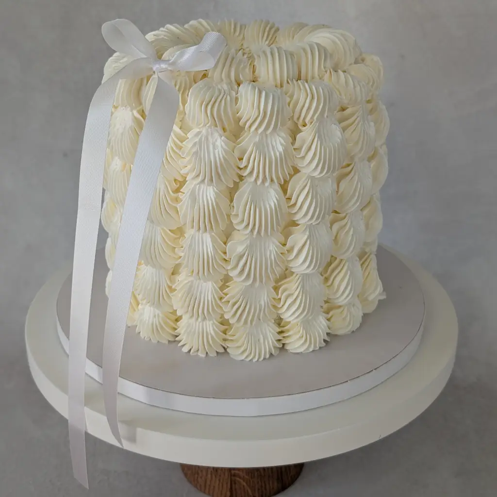 Top angle of a white buttercream cake with thick dotted buttercream dots all round on cake stand, by Nadiya's Cupcakes