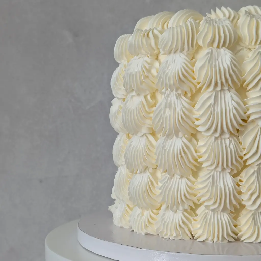 Side angle of a white buttercream cake with thick dotted buttercream dots all round, by Nadiya's Cupcakes