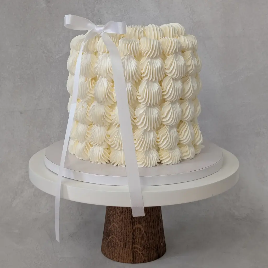White buttercream cake with thick dotted buttercream dots all round on cake stand, by Nadiya's Cupcakes