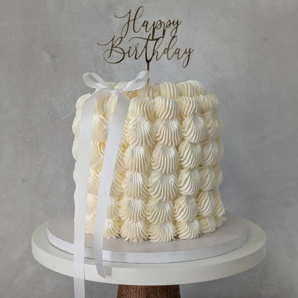 White buttercream cake with thick dotted buttercream dots all round with gold acrylic happy birthday cake topper on top, by Nadiya's Cupcakes