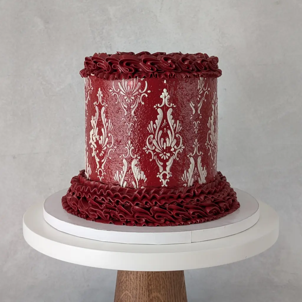 Red buttercream piped cake with white buttercream stencils on a cake stand, by Nadiya's Cupcakes