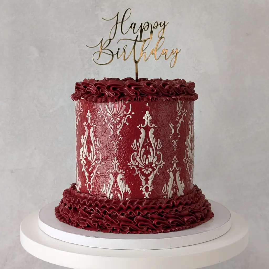 Red buttercream piped cake with white buttercream stencils with a Happy Birthday acrylic gold cake topper on a cake stand, by Nadiya's Cupcakes